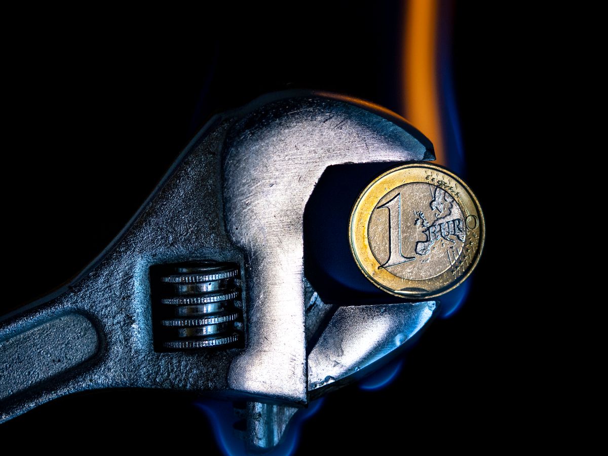 A pressure tool, the wrench catches a burning euro coin on a  white background. Concept of the high price of gas for heating and fossil fuels due to the crisis of the war in Ukraine. gas, gáz, gázársapka, 
