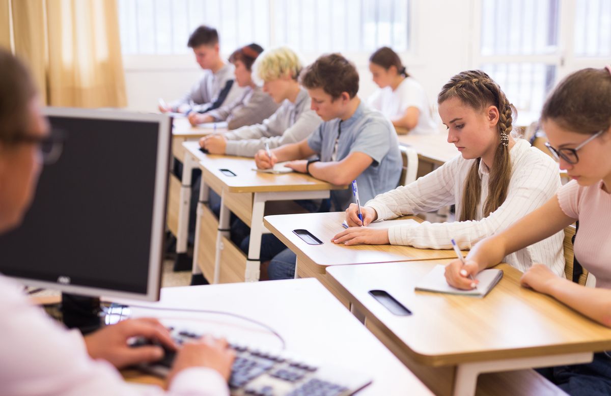 Group of teenage high school students diligently working in class, making notes of teacher lecture