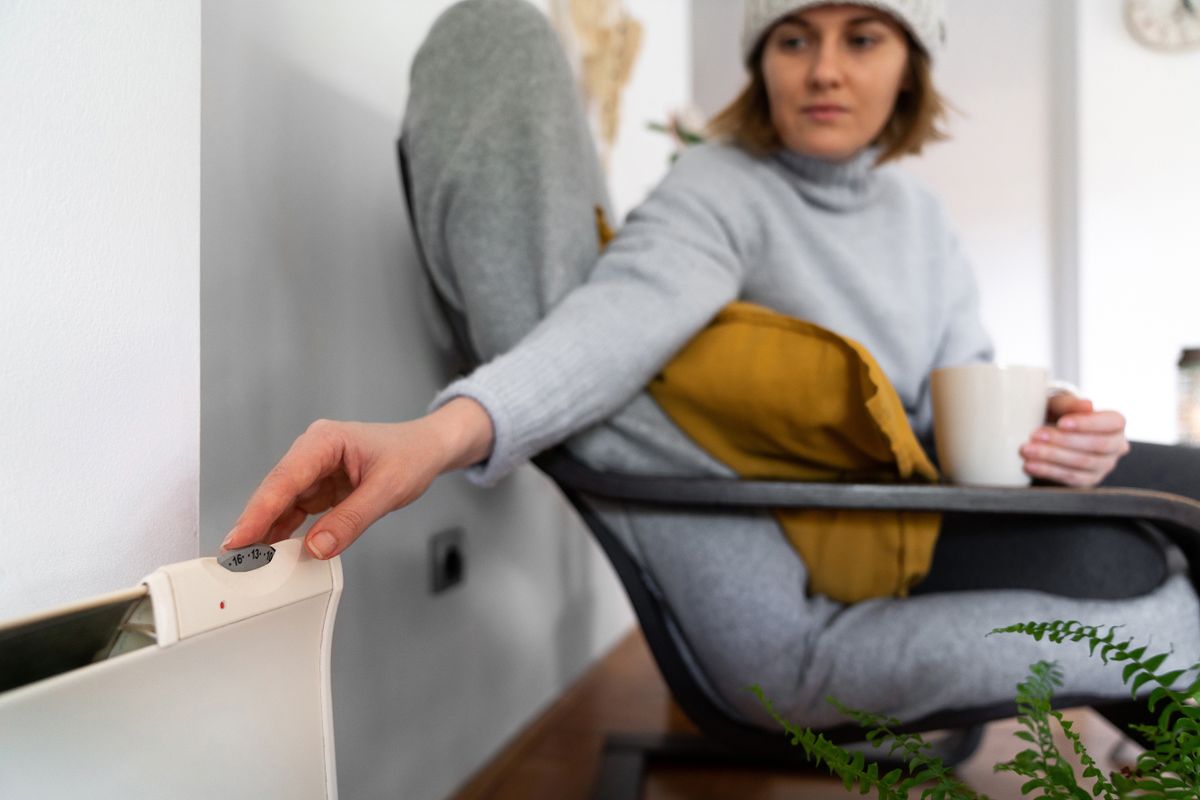 A woman in warm clothes holds her hand on the heater thermostat. Low heating temperature in the house. Energy crisis concept