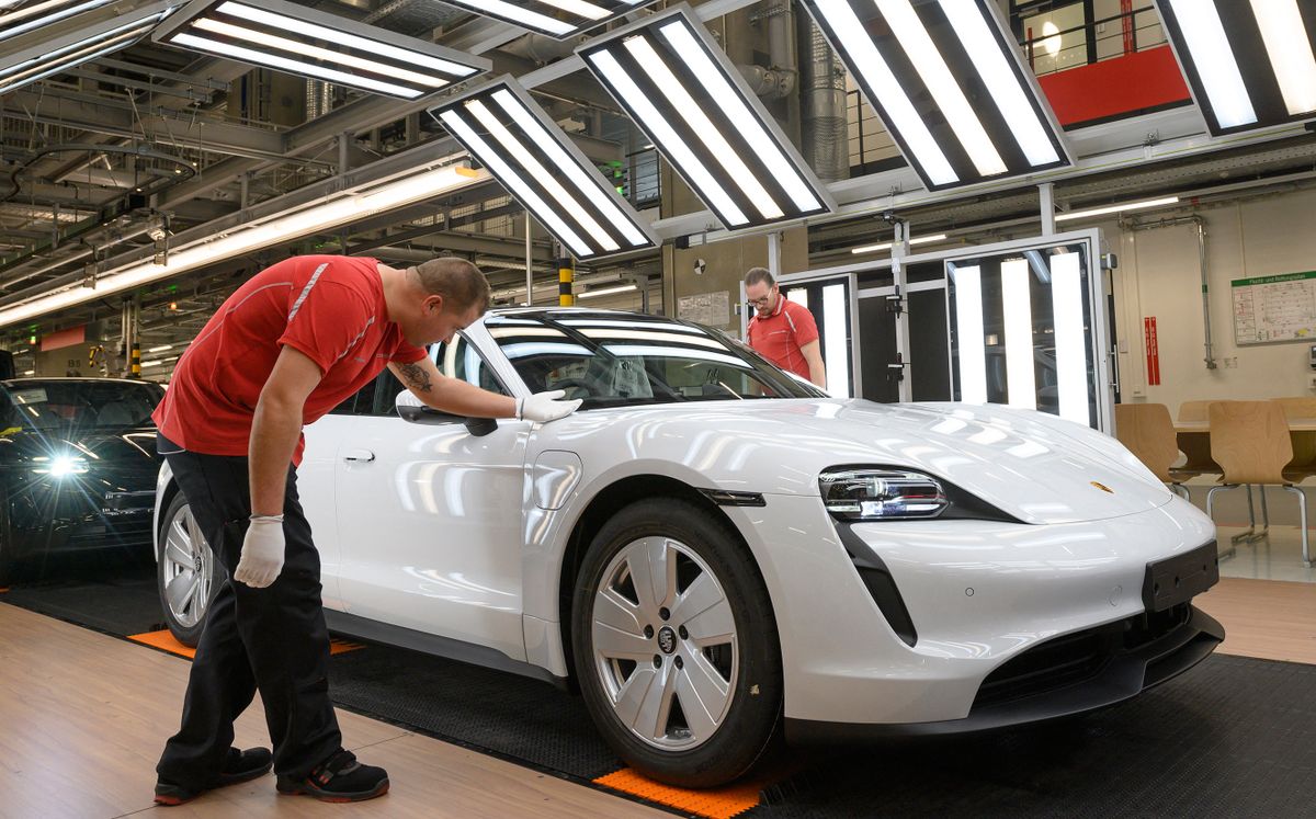 Employees of German car manufacturer Porsche AG inspect the quality of the varnish of Taycan full-electric sports cars under a light channel at the end of the assembly line at the production site in Stuttgart, southern Germany, on September 26, 2022. 