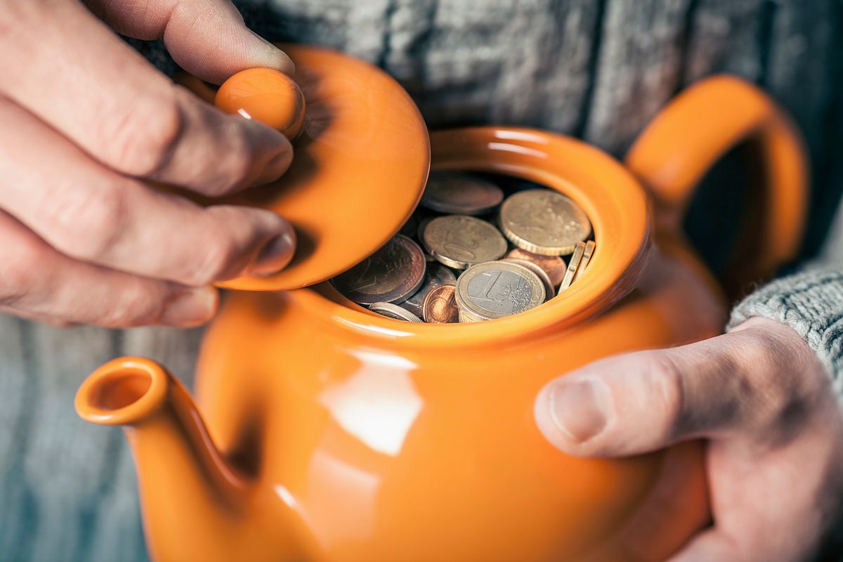 Close up of mans hands holding teapot full of coins, háztartások pénzügyi vagyona, félretett pénz, tartalék, 