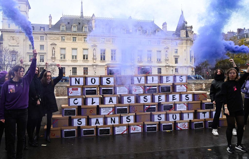 Demonstrators hold purple flare as they stand next to a wall made up of boxes of files, to symbolize the files closed without follow-up, with the inscription "our lives closed without follow-up" during a rally by the feminist collective NousToutes to protest against the inaction of the justice system in matters of sexist and sexual violence, in front of the Palais de Justice, the historical courthouse located in the Île de la Cite in Paris, on November 23, 2022. (Photo by Bertrand GUAY / AFP)