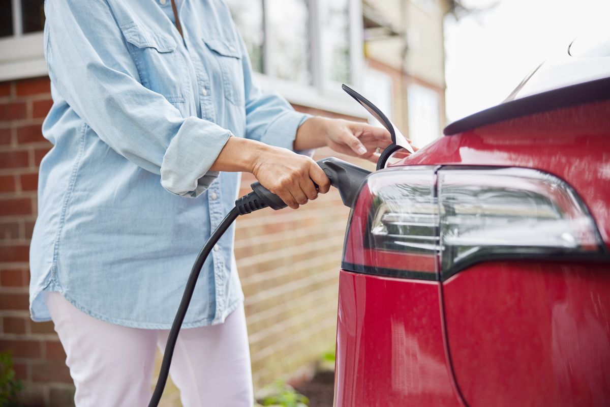 Close Up Of Woman Attaching Charging Cable To Environmentally Friendly Zero Emission Electric Car At Home, Close Up Of Woman Attaching Charging Cable To Environmentally Friendly Zero Emission Electric Car At Home