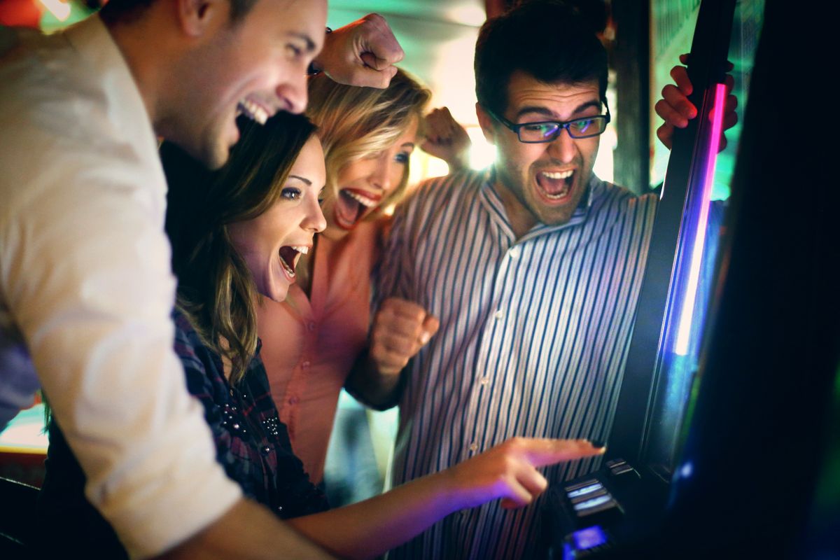 Group of young adults having fun in casino. Group of young adults in late 20's playing slot poker and fruits and wining.Wearing casual clothes and having fun on weekend night. There are many slot machines out of focus in background.