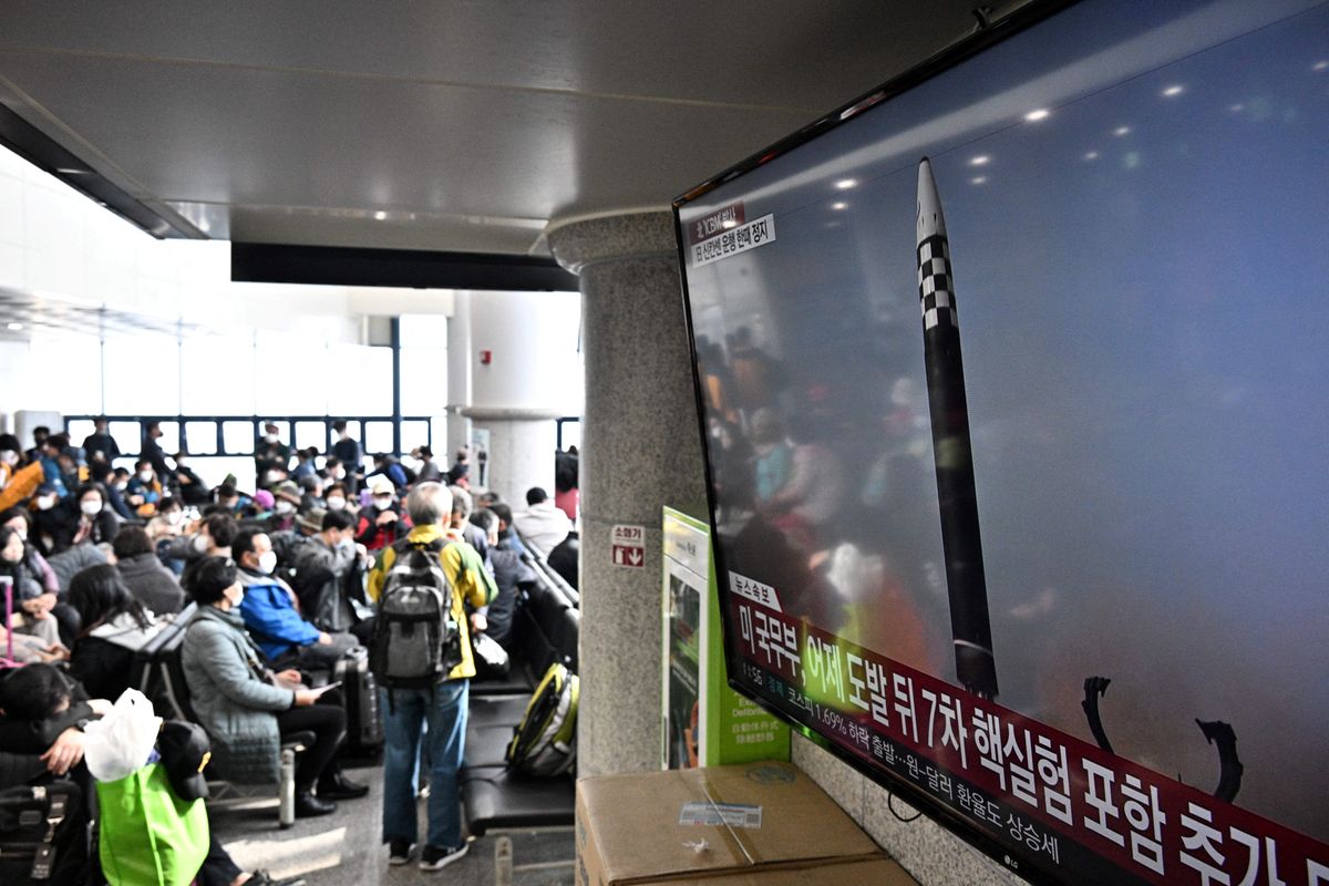 Passengers at a ferry terminal ferry sit near a television showing a news broadcast with file footage of a North Korean missile test.
