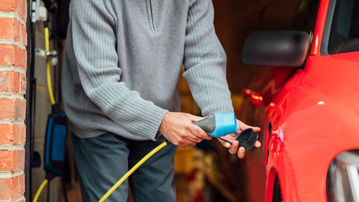Using Electricity For Travel, A front view of an unidentifiable male charging his red electric car at his home charging point., 