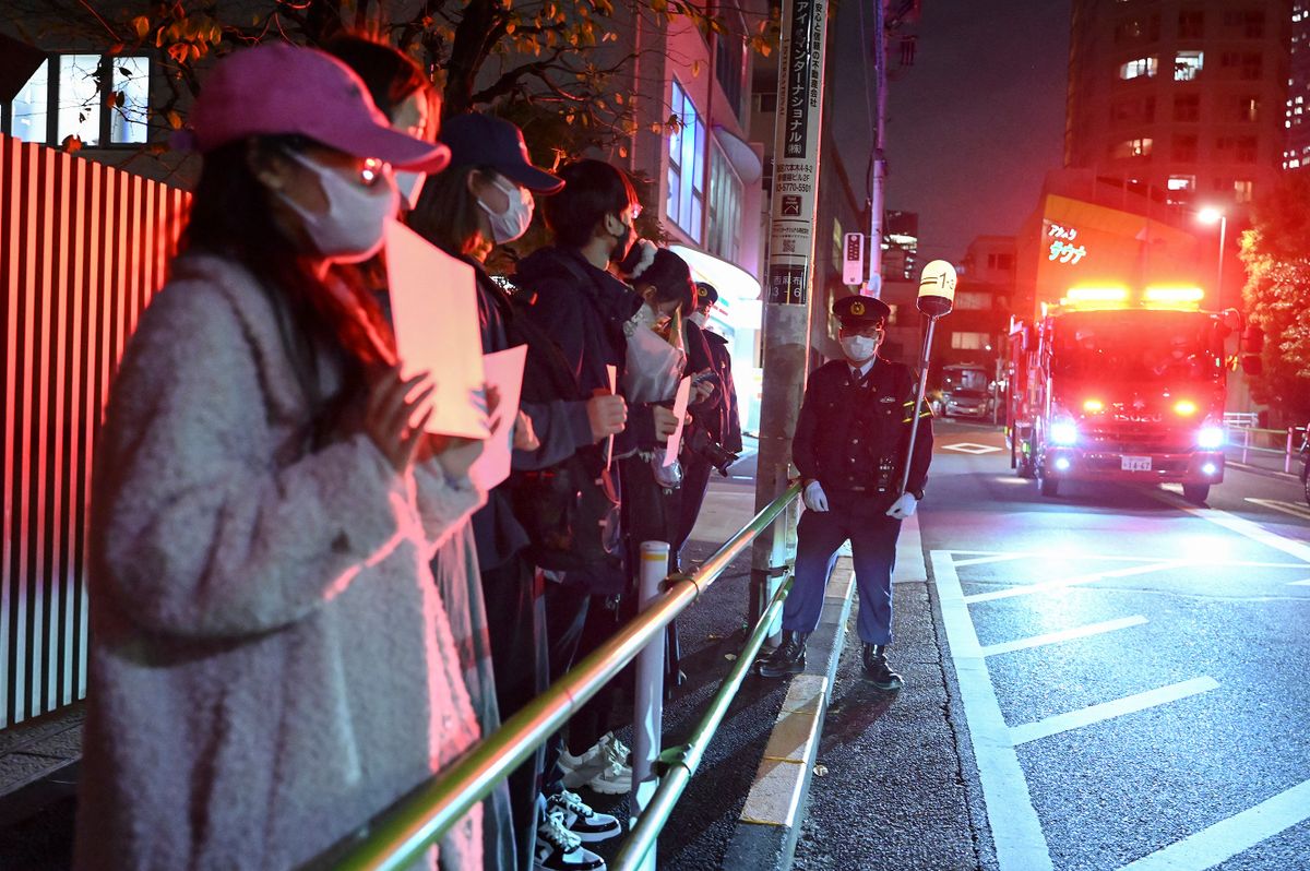 A fire truck (R) passes as a small group of protesters (L) hold up blank white pieces of paper in protest directly across the street from the Chinese embassy in Tokyo on November 28, 2022, in support of demonstrations held in China over Beijing's Covid-19 restrictions. - Hundreds of people have taken to the streets in China's major cities in a rare outpouring of public anger against the state over its zero-Covid policy. (Photo by Richard A. Brooks / AFP)