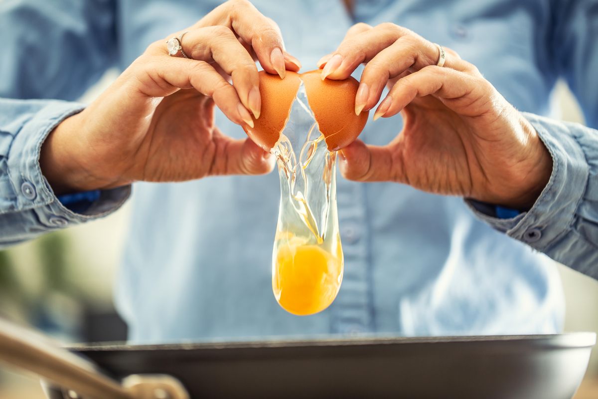 A detail of cracked egg falling into the pan as woman holds egg shells in both hands. A detail of cracked egg falling into the pan as woman holds egg shells in both hands. tojás