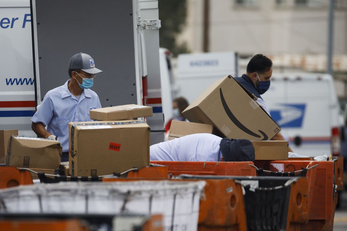 An Amazon.com Inc. package sits in a cart as U.S. Postal Service employees load mail and packages into a delivery vehicle outside a post office in Torrance, California, U.S., on Monday, Aug. 17, 2020. A pitched battle over the USPS and its ability to reliably deliver presidential election ballots during a pandemic has broken out on the eve of the parties' high-profile conventions. 