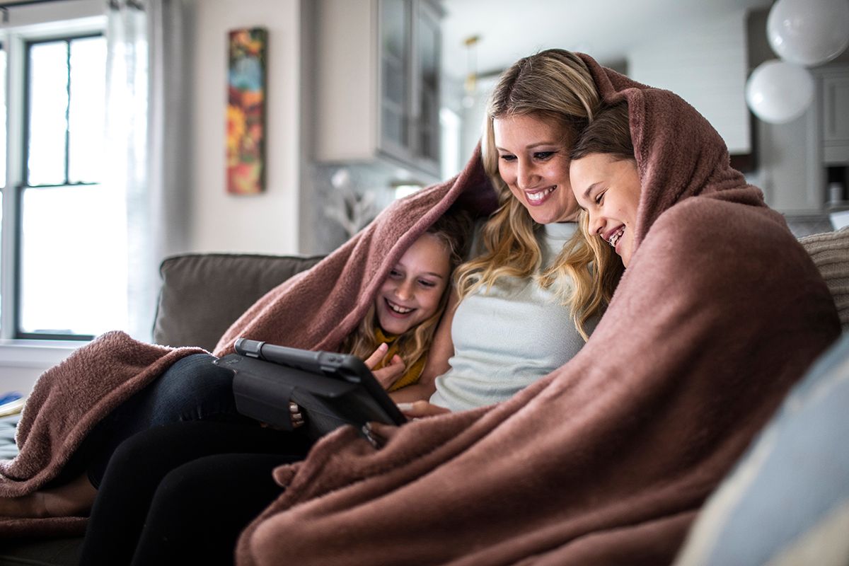 Mother and tween daughters snuggled under blanket and watching a movie on digital tablet Mother and tween daughters snuggled under blanket and watching a movie on digital tablet