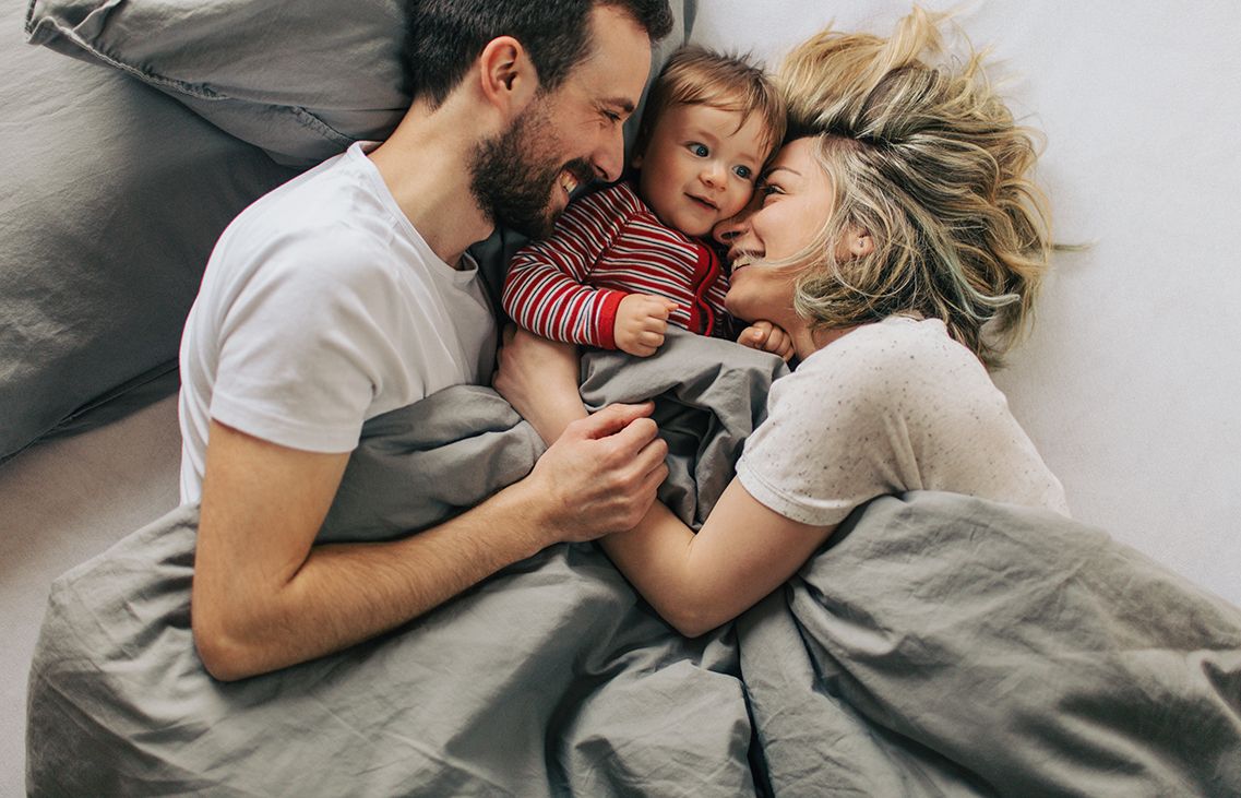 Morning routine with our baby boy Photo of young parents enjoying morning routine in a cosy bed with their baby boy. Magyar családpolitika.