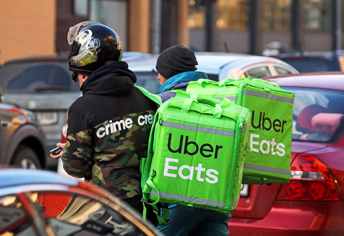 Delivery,Men,Carry,Food,In,Uber,Eats,Green,Boxes,On, delivery men carry food in Uber Eats green boxes on a street.