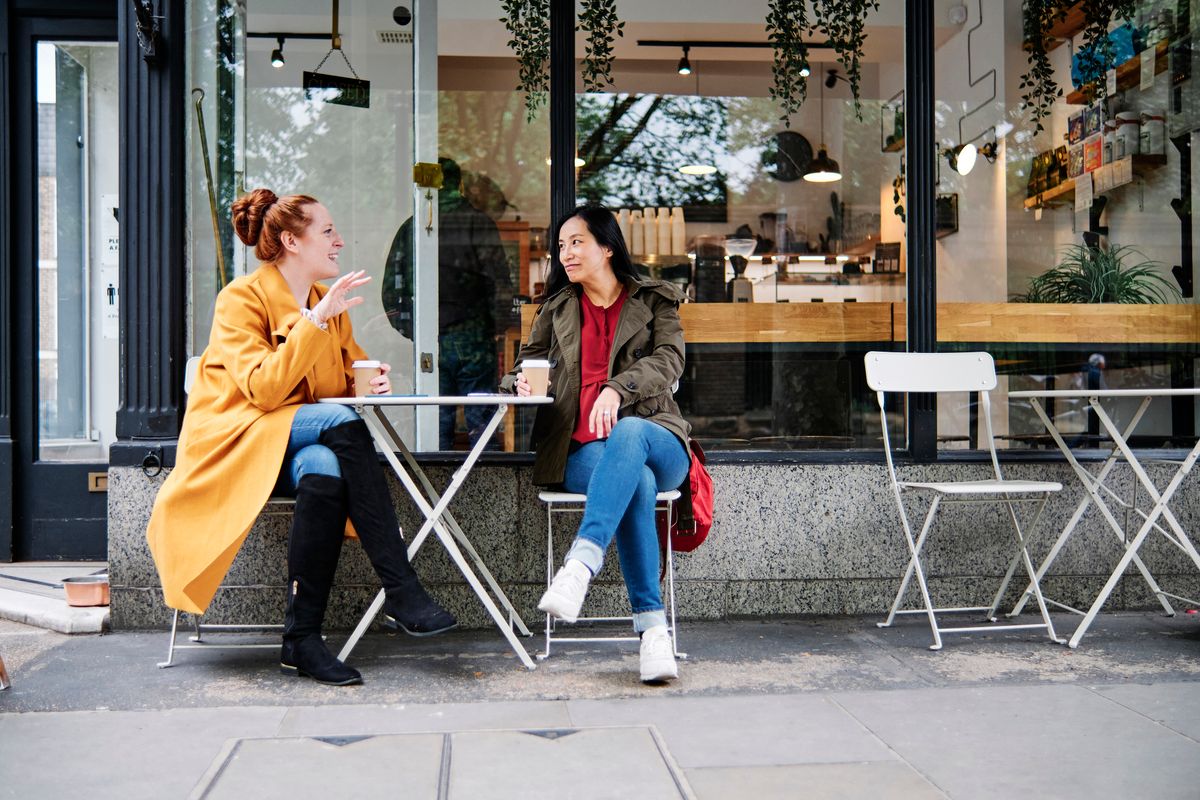 Woman gesturing while talking with female friend outside coffee shop, Friends hanging out and having a good time in a cafe. London, Engalnd.