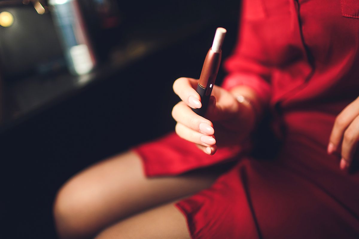 Electronic,Cigarettes,,Technology,Cigarette.,Tobacco,System,Iqos.,Female,Hand,On Electronic cigarettes, technology cigarette. Tobacco system IQOS. Female hand on blurred background of the restaurant. red case.