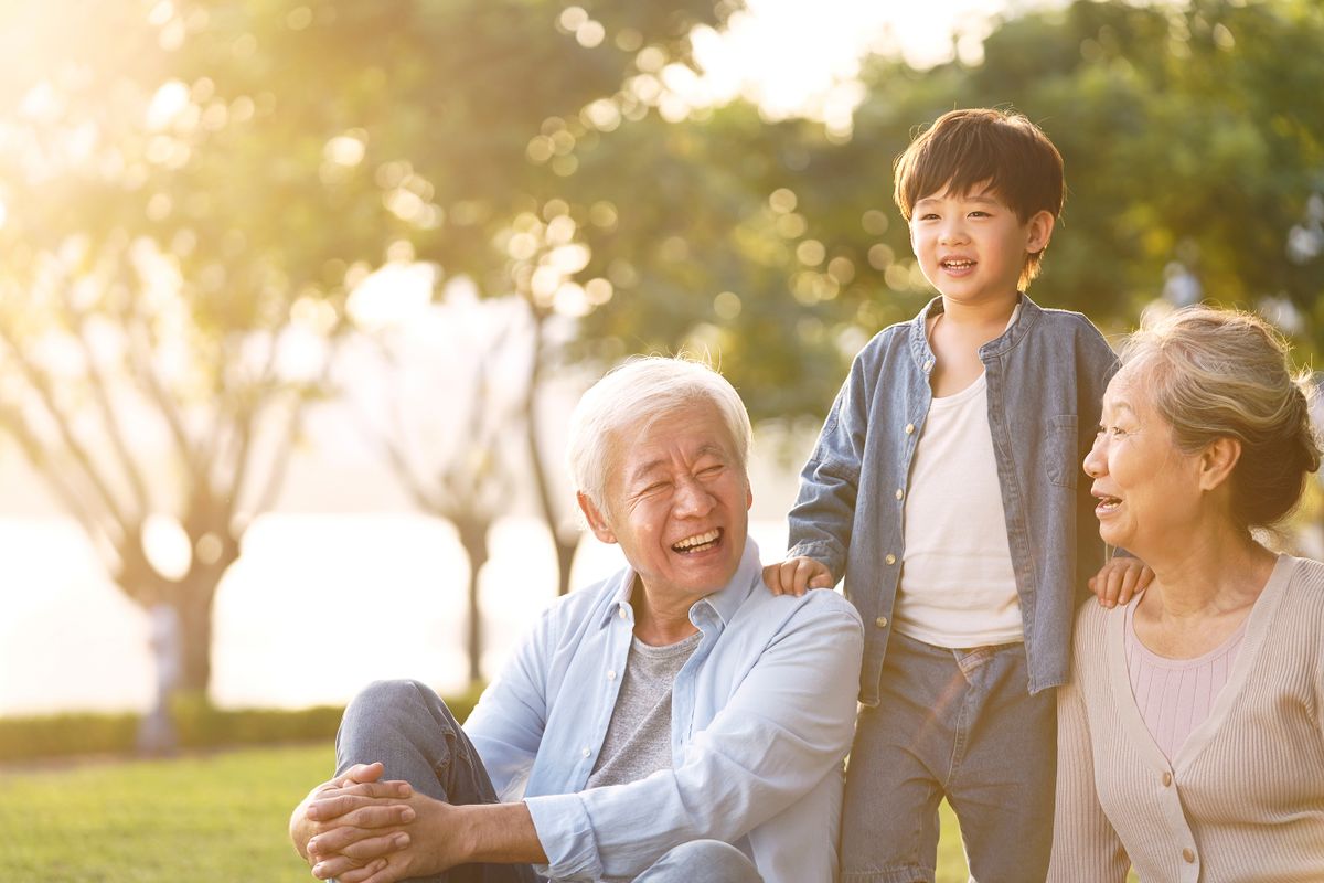 Asian,Grandson,,Grandfather,And,Grandmother,Sitting,Chatting,On,Grass,Outdoors