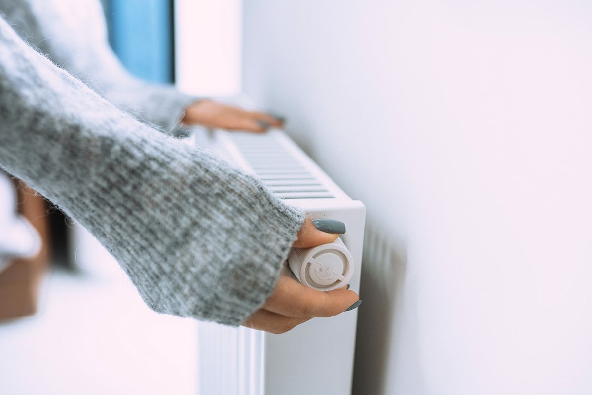Economic crisis and despair in cold houses. Control thermostat temperature on radiator Unrecognizable woman hands in gray sweater touching and setting radiator thermostat regulator