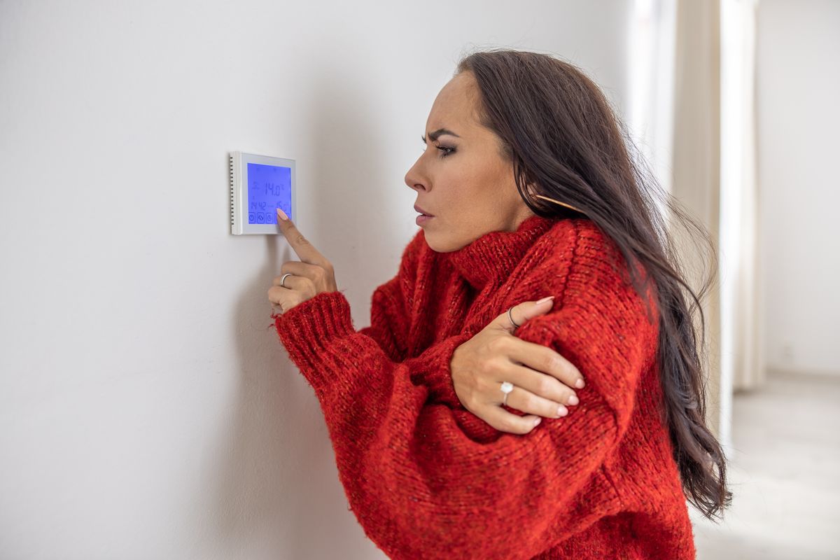Freezing woman at home wears sweater and tries to raise the temperature on thermostat while energy crisis hits Europe in the winter.