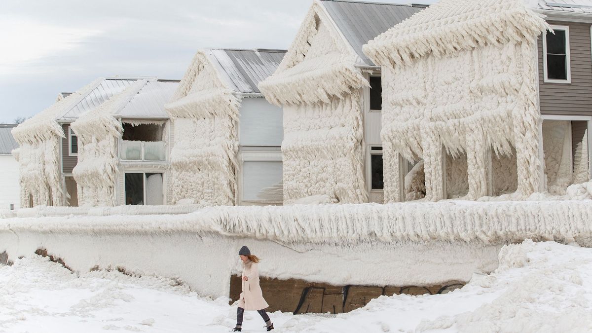 A person walks by homes covered in ice at the waterfront community of Crystal Beach in Fort Erie, Ontario, Canada, on December 28, 2022, following a massive snow storm that knocked out power in the area to thousands of residents.