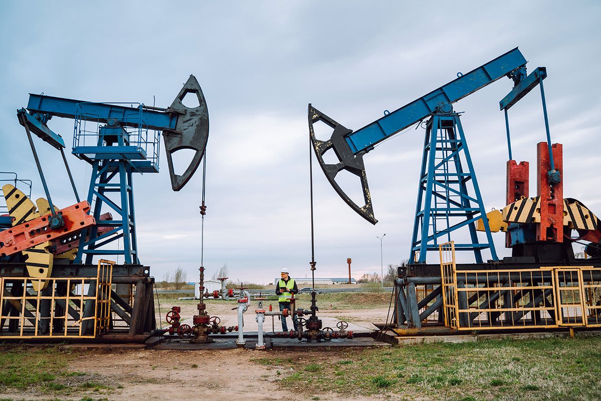 Oil pumps, nodding donkey or pump jack and rig against blue cloudy sky. Geologist engineer in protective wear staying in between construction Onshore oil and gas well in the field outdoors against cloudy sky