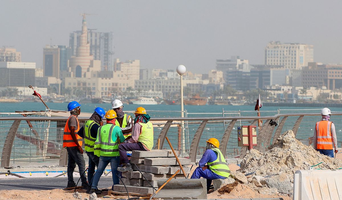 A picture taken on May 21, 2022, shows workers fixing a sidewalk with a backdrop of the Qatari capital Doha, six months ahead of the FIFA World Cup 2022 which the country is hosting. 
Katari vb