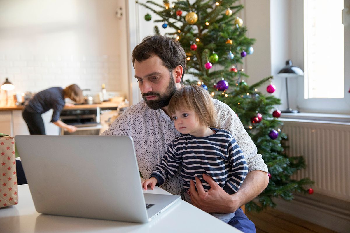 Father and toddler daughter doing christmas shopping online while sitting at table in front of christmas tree Caucasian man holding his one year old daughter while using laptop in front of christmas tree