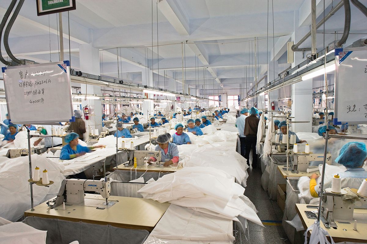 Textile workers in long rows at sewing machines making clean suits.
