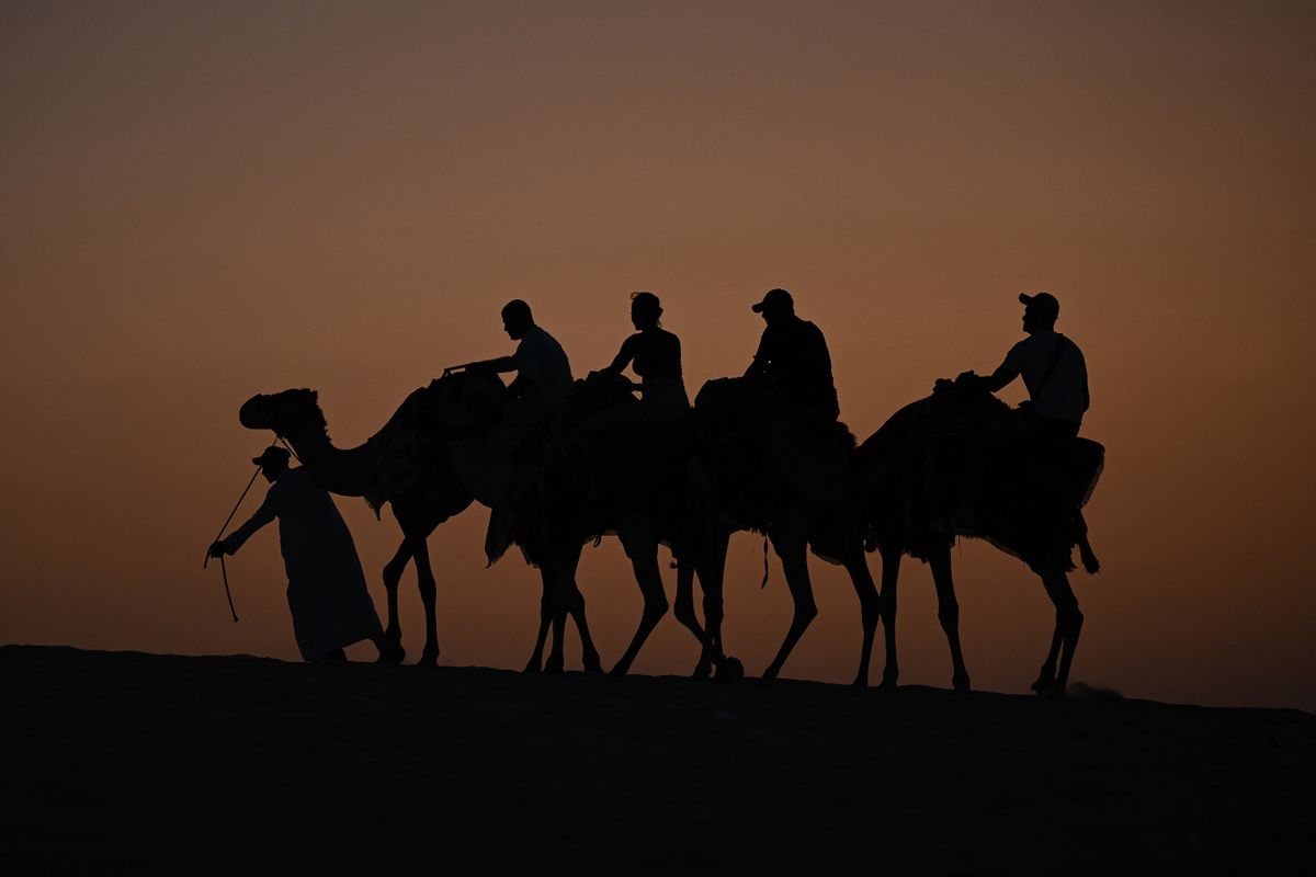 Tourists ride camels in a desert, some 50 km off the Qatari capital of Doha in the direction of Saudi Arabia, on December 2, 2022, during the Qatar 2022 World Cup football tournament. 