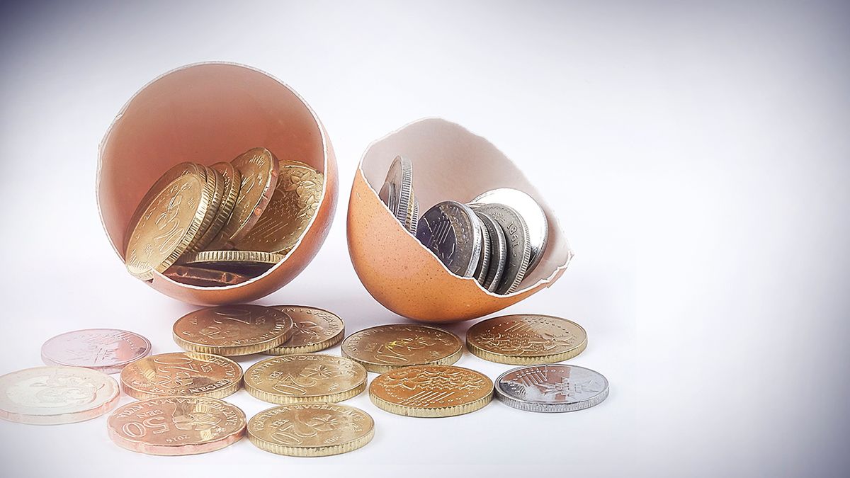 Close-Up Of Coins In Broken Eggshell Against White Background Egg shell and coins with investment and business text conceptual. befektetés, kamat, kincstárjegy, MNB,mnb,