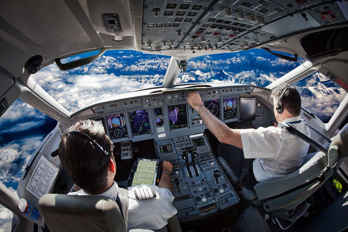 Cockpit,Of,The,Modern,Passenger,Aircraft,In,Flight.,Pilots,FlyCockpit of the modern passenger aircraft in flight. Pilots fly an airplane over the mountain landscape. Blue cloudy sky is visible outside the cockpit.