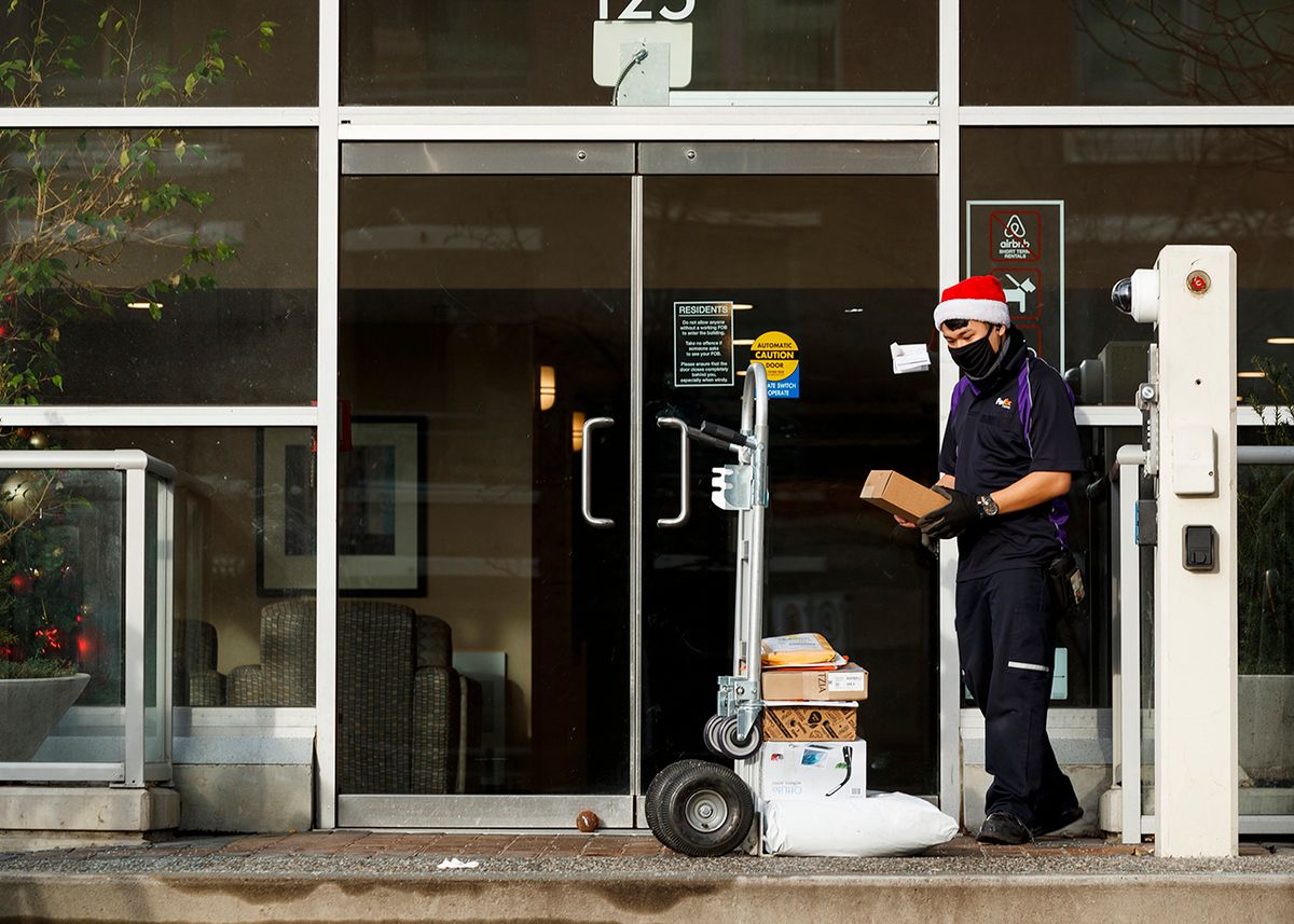 Holiday Season In Vancouver, VANCOUVER, BRITISH COLUMBIA - DECEMBER 24: A FedEx employee wearing a Santa hat sorts the parcels on his hand truck at the entrance of an apartment on December 24, 2020 in Vancouver, Canada.  (Photo by Andrew Chin/Getty Images)