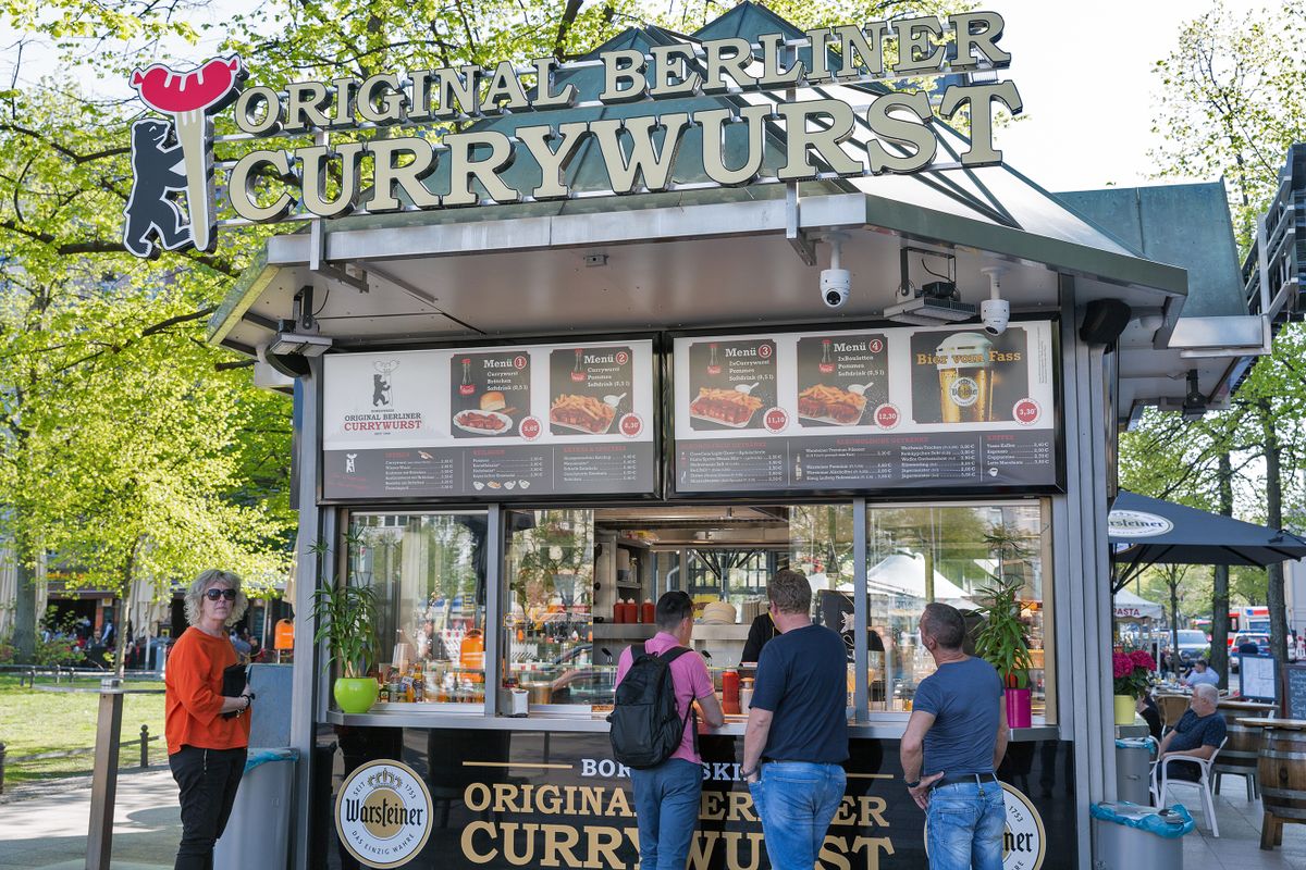 BERLIN, GERMANY - APRIL 18, 2019: People visit Original Berliner Currywurst, curry sausage fast food outdoor cafe on Wittenberg square. Berlin is the capital and largest city of Germany.