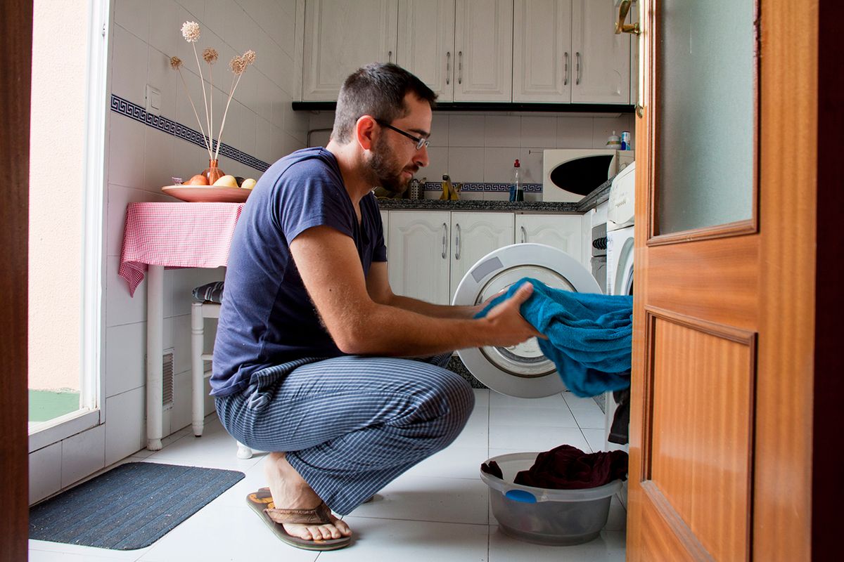 Man in kitchen, lakossági, áramfelhasználás, energia, áram, rezsi, Close-up of man wearing blue pijama pulling towel from washing machine in kitchen.