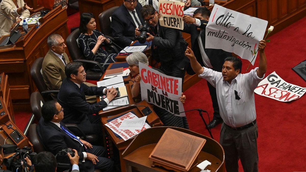 Peruvian congressmen and women protest holding banners upon the entrance of the Peru's chief of staff Alberto Otarola (seated bottom left), at the beginning of the plenary session of the Congress in Lima on January 10, 2023. - Protests against Peru's president, Dina Boluarte, which have left 40 people dead in a month, continue on Tuesday with road blockades in six regions of the country as the new cabinet goes to the Congress to ask for a vote of confidence in its inauguration. 