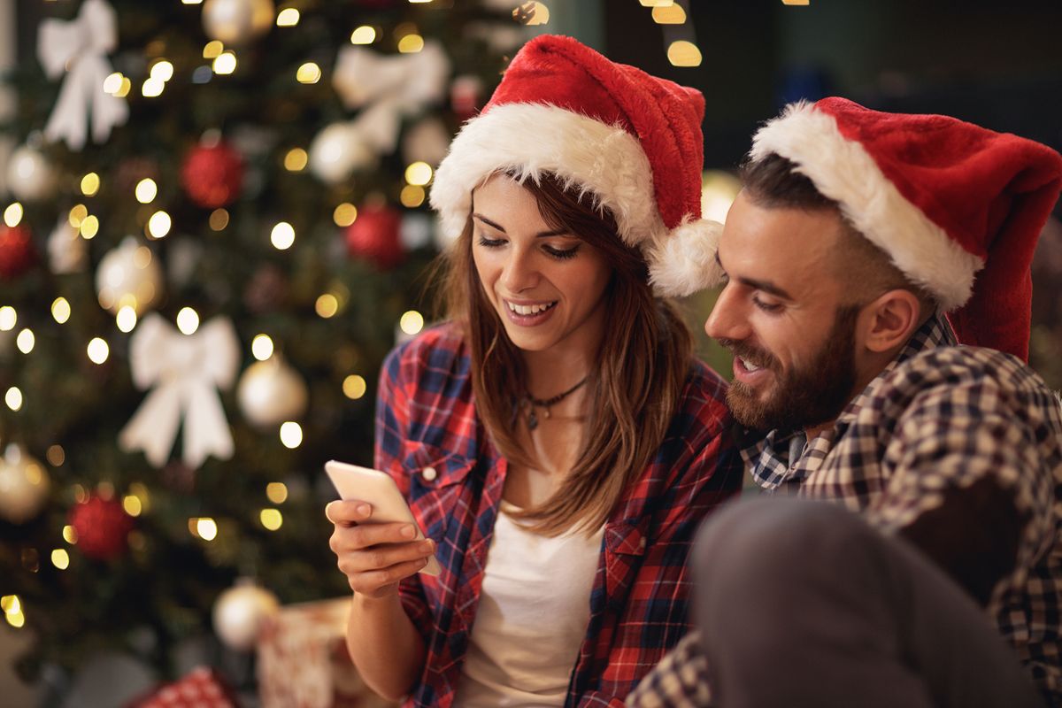 Young,Couple,On,Christmas,Eve,Looking,At,Cell,Phone,Together