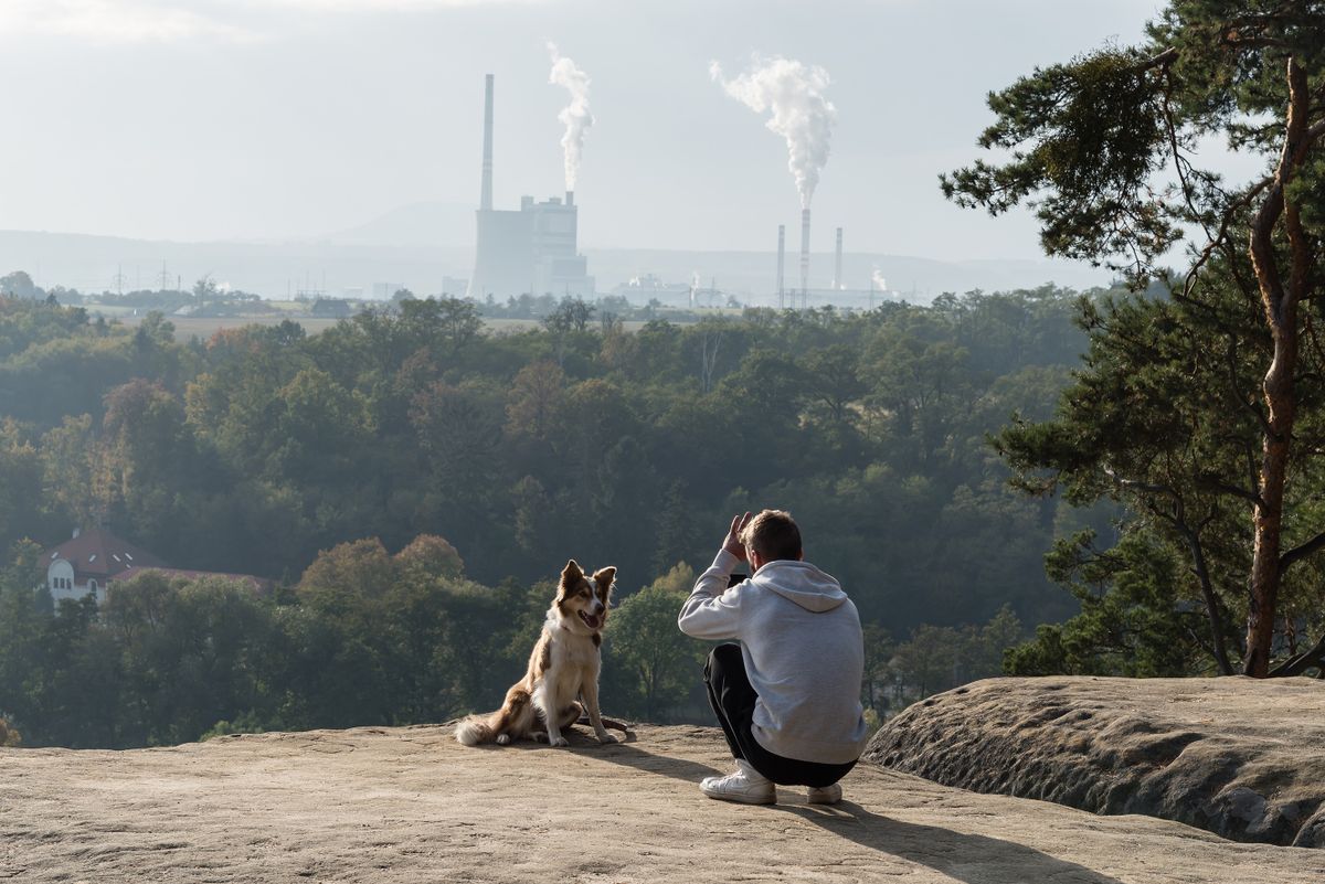 MELNIK, CZECH REPUBLIC - 2021/10/17: Man taking photo of his dog on the rock with view of power plant Melnik, which is operated by company CEZ, biggest power producer in Czech republic. The power plant is located on the north approx. 36 kilometers from Czech capital Prague. Due to the significant growth of energy price on market several independent distributors of electrical energy (including Bohemia Energy and Kolibrik energie) in Czech republic have gone bankrupt in the past week. 