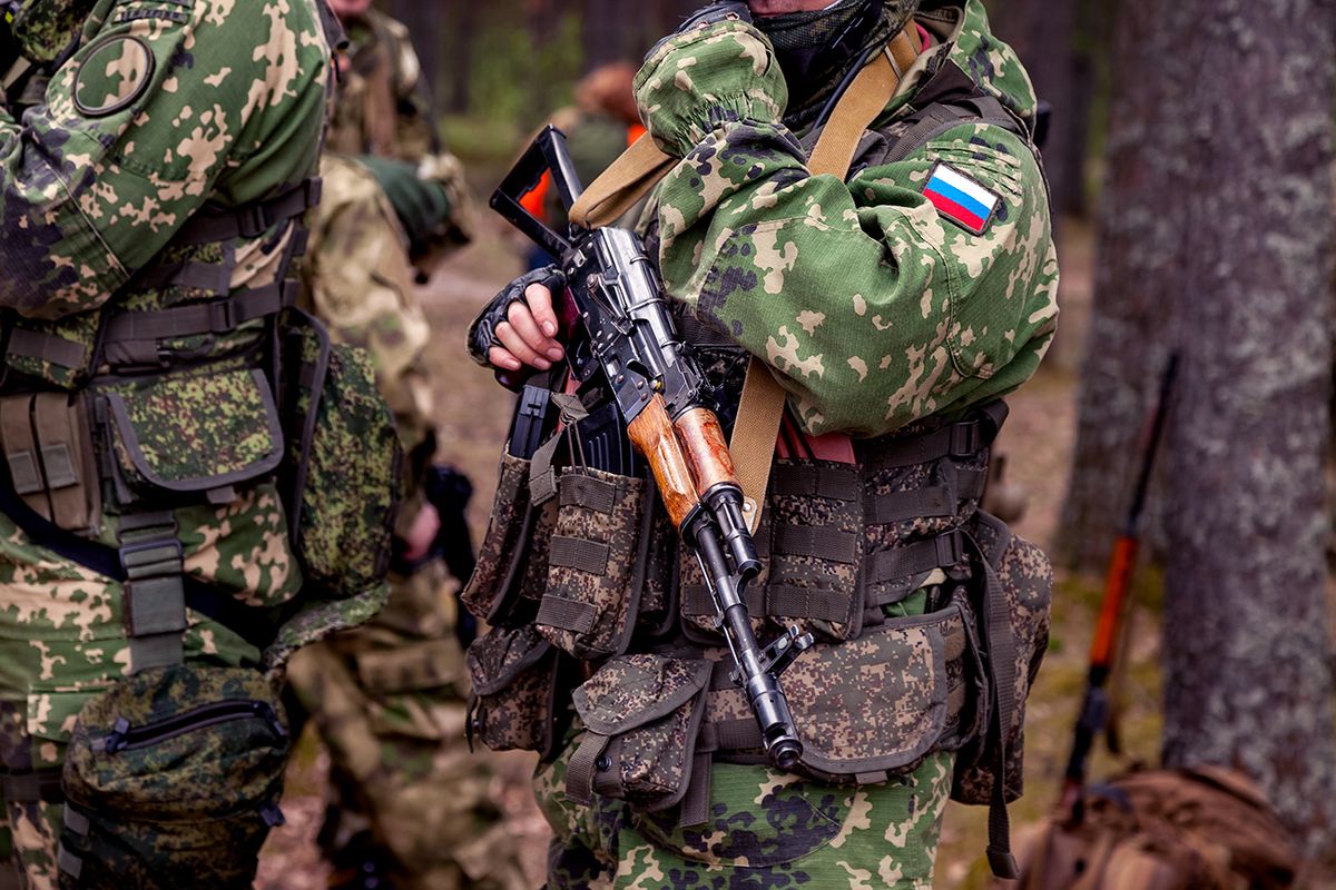 Close up hands russian soldier man dressed military camouflage uniform holds weapon in woodland at soldiers background. Male  Close up hands russian soldier man dressed military camouflage uniform holds weapon in woodland at soldiers background. Male border guard in country border holding machine gun on war. Copy text spaceborder guard in country border holding machine gun on war. Copy text space