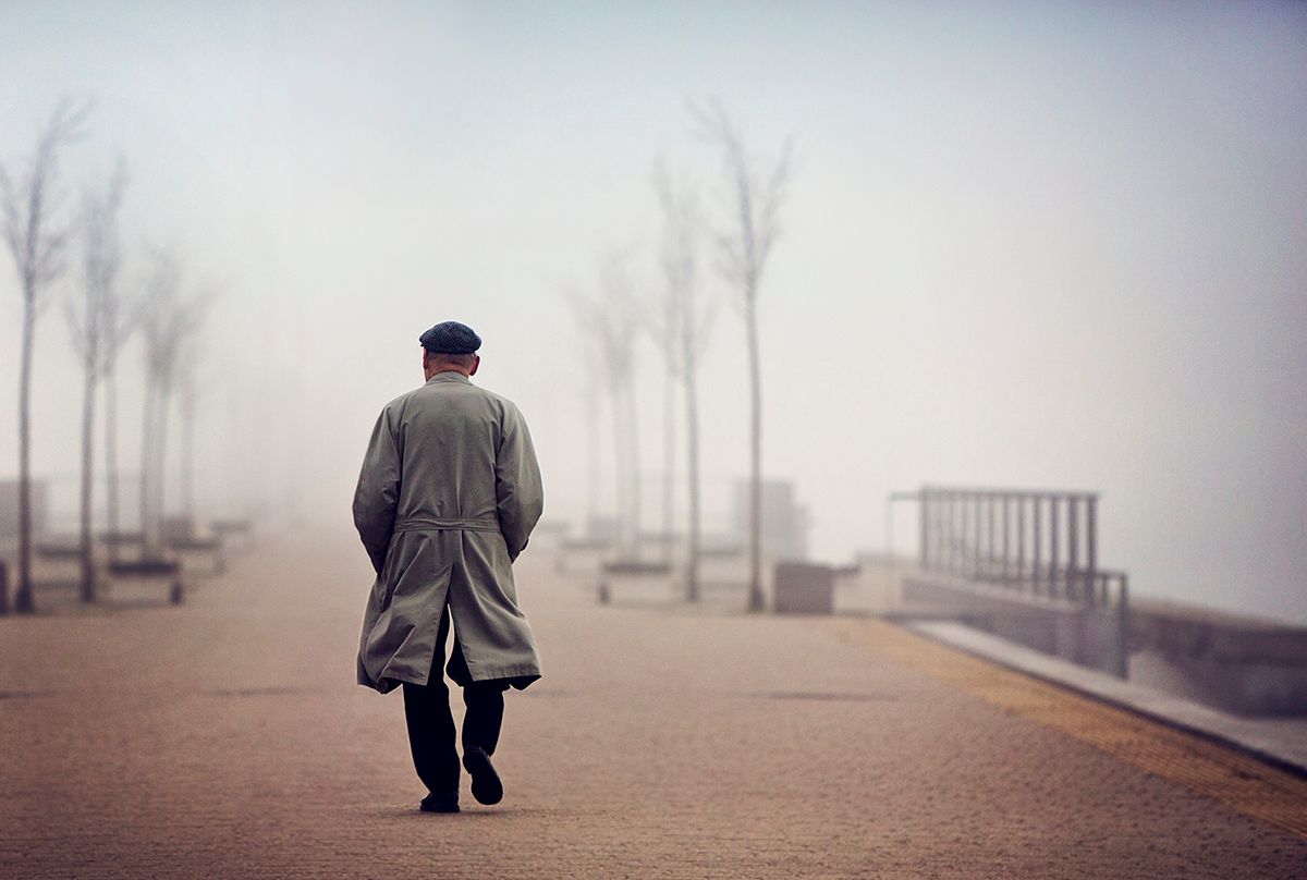 Old man walking down empty foggy road