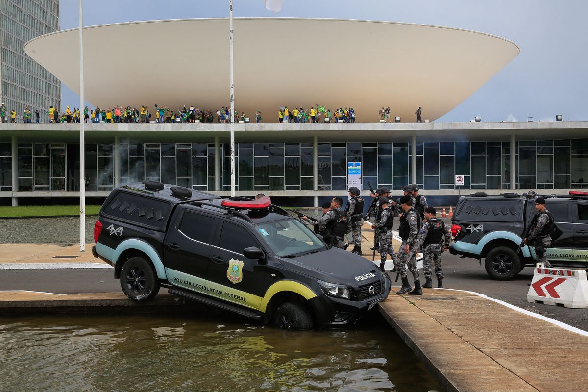 Members of the Federal Legislative Police stand next a vehicle that crashed into a fountain as supporters of Brazilian former President Jair Bolsonaro invade the National Congress in Brasilia on January 8, 2023. - Hundreds of supporters of Brazil's far-right ex-president Jair Bolsonaro broke through police barricades and stormed into Congress, the presidential palace and the Supreme Court Sunday, in a dramatic protest against President Luiz Inacio Lula da Silva's inauguration last week. 