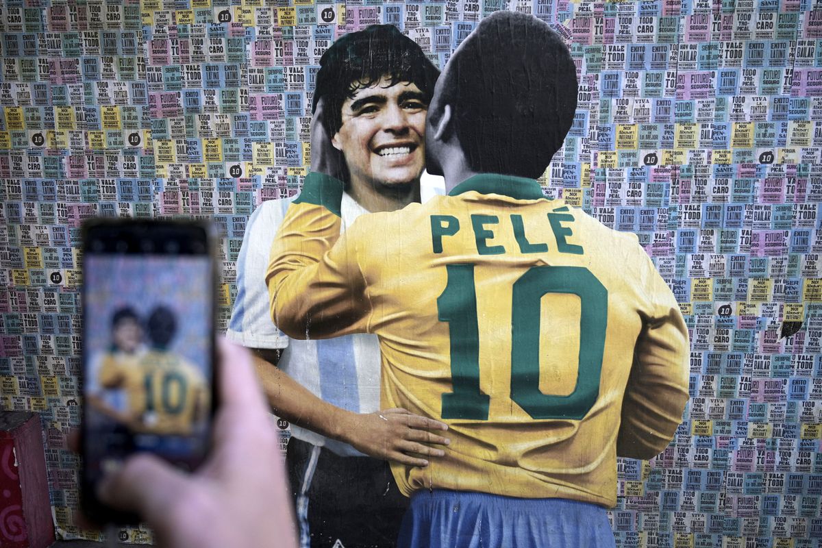 A man takes a picture of a wall depicting an image of late football stars Diego Maradona of Argentina and Pele of Brazil embracing each other, in Buenos Aires on December 29, 2022, just hours after the passing of Pele