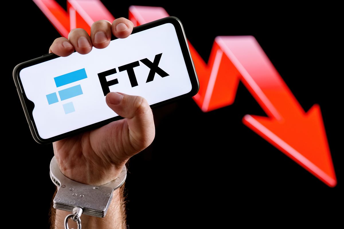 Kazan, Russia - Nov 14, 2022: FTX is cryptocurrency exchange. Handcuffed hand squeeze smartphone with FTX logo on screen against background of red down arrow.