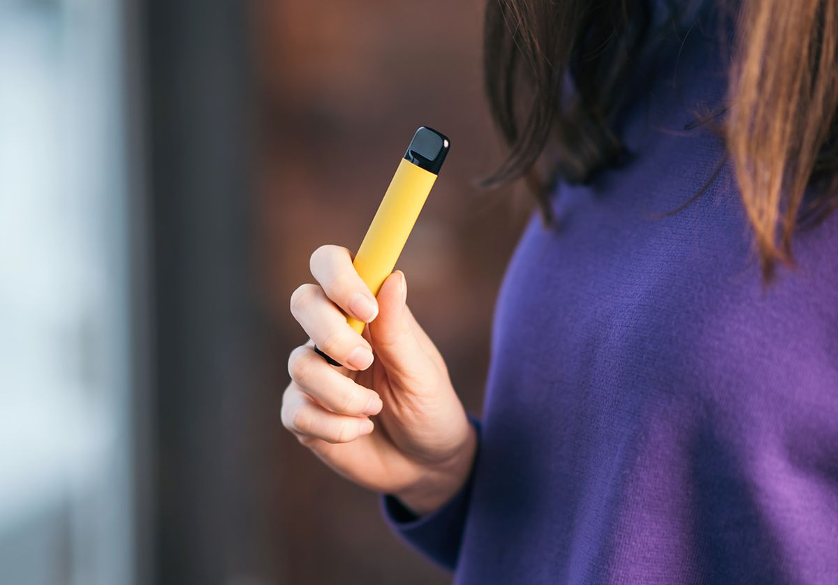 Yellow,Disposable,Electronic,Cigarette,In,A,Woman's,Hand.,Modern,Smoking Yellow disposable electronic cigarette in a woman's hand. Modern smoking 