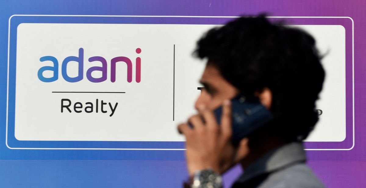 A man talks on his phone walks past an Adani logo in Mumbai, India, 23 November, 2022. Adani Group's Founder &amp; Chairman on Saturday claimed that India will become the world's third-largest economy by the end of 2030 and the country will become 2nd largest economy by 2050 according to an Indian media report.    