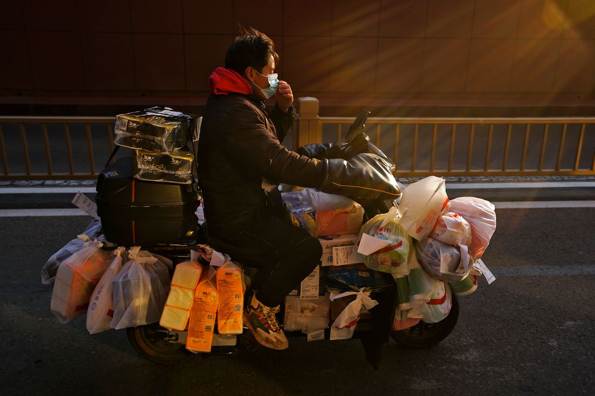 Peking, 2023. január 4.Házhozszállítást végző motorkerékpáros futár megigazítja védőmaszkját Pekingben 2023. január 4-én. Kínában december 7-én váratlanul feloldották az egészségügyi és kijárási korlátozásokat, ami négy hét alatt a koronavírusos betegek és áldozatok számának drámai növekedéséhez vezetett.