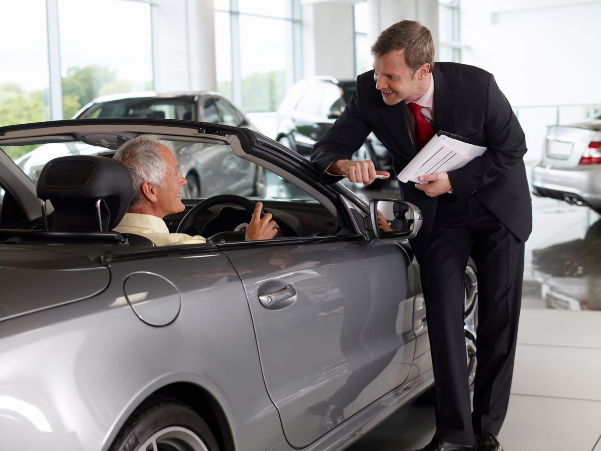 Salesman talking to man in convertible in automobile showroom