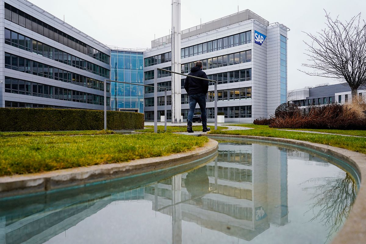 Software group SAP - annual figures 26 January 2022, Baden-Wuerttemberg, Walldorf: A man walks across a bridge in front of the main building of the software company SAP by a watercourse in which the building is reflected. On Thursday (Jan. 27), the company will announce its financial figures for the past year. Photo: Uwe Anspach/dpa (Photo by Uwe Anspach/picture alliance via Getty Images)