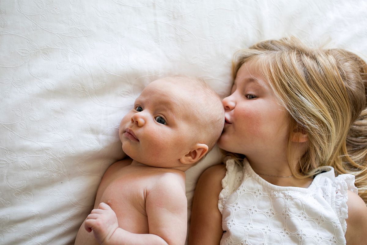 Overhead view of young girl and baby brother lying on bed, girl kissing baby brother, babaváró hitel