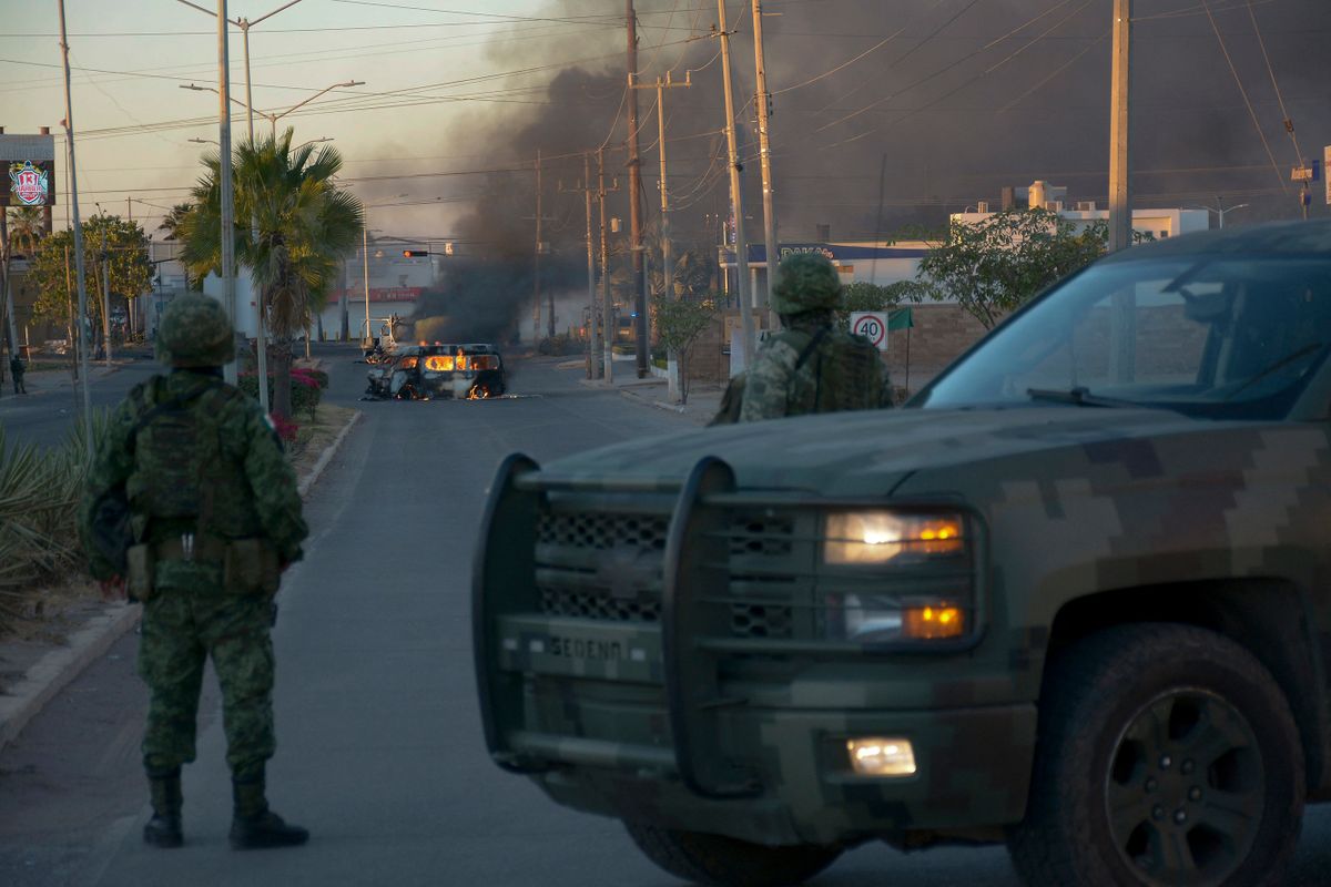 Mexicans soldiers stand guard near burning vehicles on a street during an operation to arrest the son of Joaquin "El Chapo" Guzman, Ovidio Guzman, in Culiacan, Sinaloa state, Mexico, on January 5, 2023. - Mexican security forces on Thursday captured a son of jailed drug kingpin Joaquin "El Chapo" Guzman, scoring a high-profile win in the fight against powerful cartels days before US President Joe Biden visits. Ovidio Guzman, who was arrested in the northwestern city of Culiacan, is accused of leading a faction of his father's notorious Sinaloa cartel, Defense Minister Luis Cresencio Sandoval told reporters. 