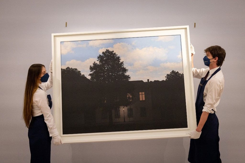 Gallery assistants pose with an artwork entitled 'L'empire des lumieres,1961' by Belgian artist Rene Magritte, during a photocall ahead of a sale of Modern and Contemporary Art, at Sotheby's auction house in London on February 22, 2022. - The artwork is expected to realise in excess of GBP 45 million (EUR 54 million, USD 61million). 