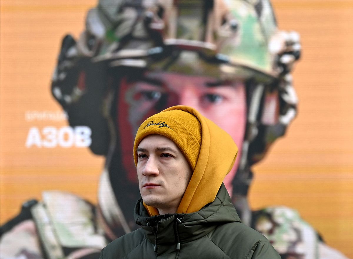 A man stands next to a placard depicting a Ukrainian soldier which reads as "Azov" in Kyiv on February 22, 2023, two days before of the first anniversary of the Russian invasion to Ukraine.