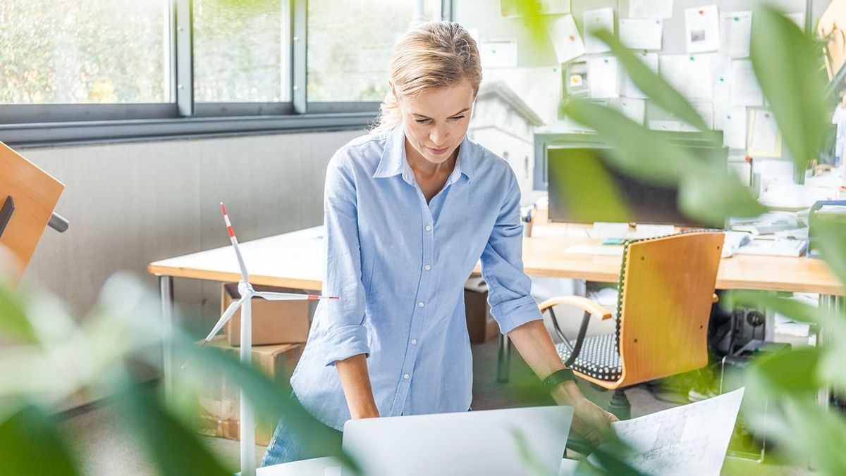 Woman in office with plan, laptop and wind turbine model on table Woman in office with plan, laptop and wind turbine model on table